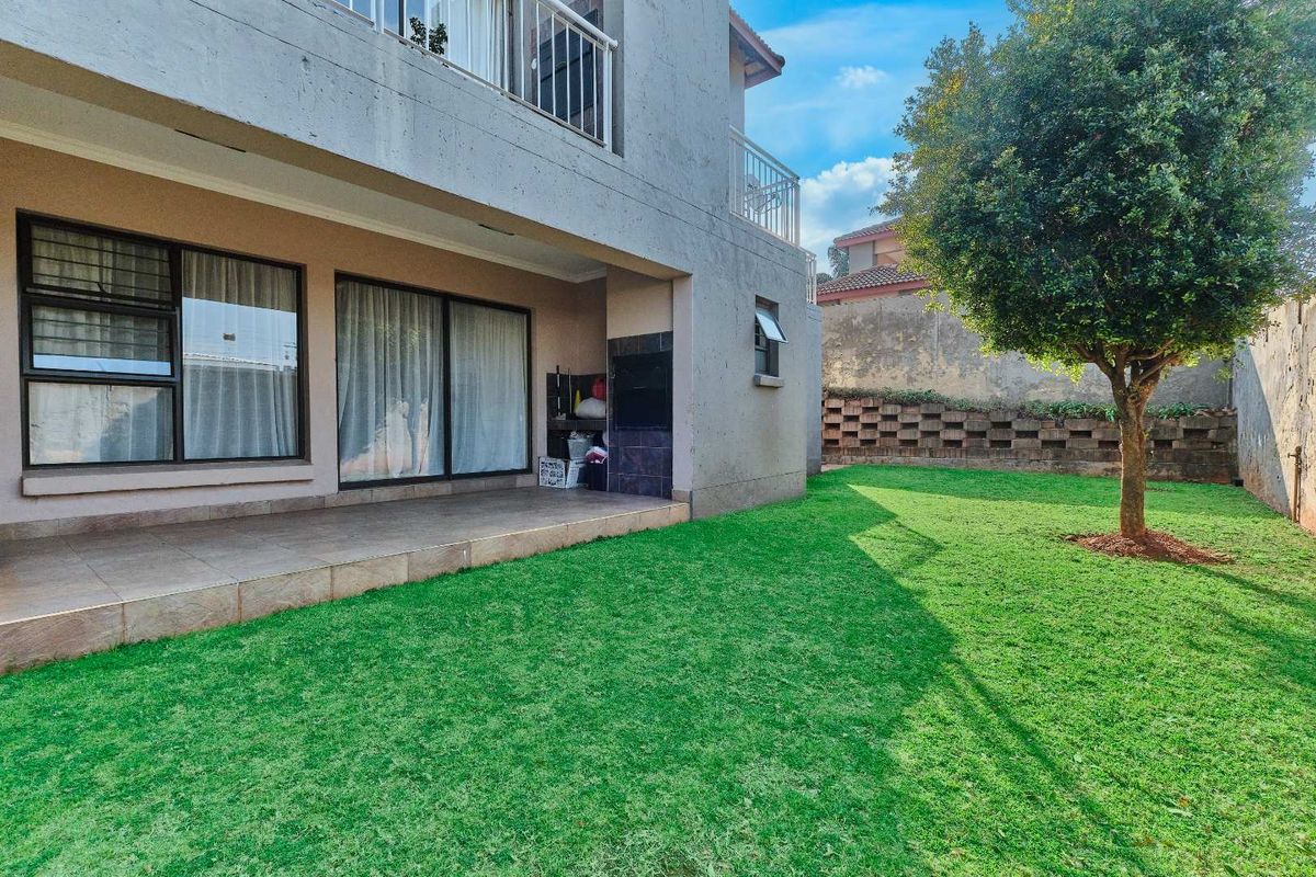 Rear exterior view of the townhouse featuring a covered tiled patio with a built-in braai, overlooking a private garden with a lawn.