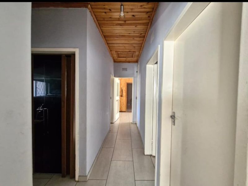 A functional hallway featuring ceramic floor tiles and a timber tongue and groove ceiling, providing access to multiple rooms within the home.