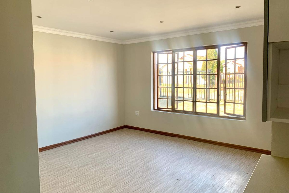 A bright and spacious living area featuring neutral walls, laminate flooring, and large timber-framed windows that provide ample natural light.