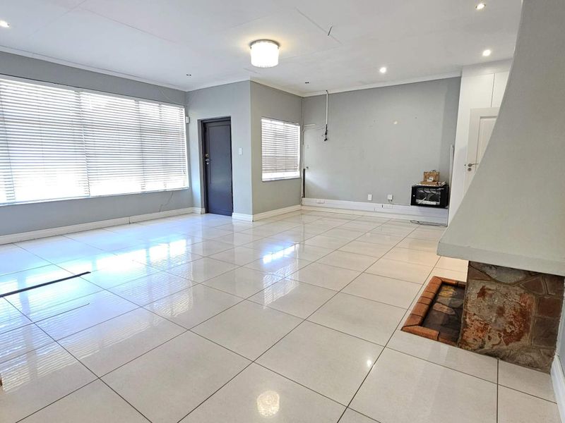 Spacious, empty living room featuring large format floor tiles, a traditional fireplace, and neutral wall finishes with natural light from large windows.