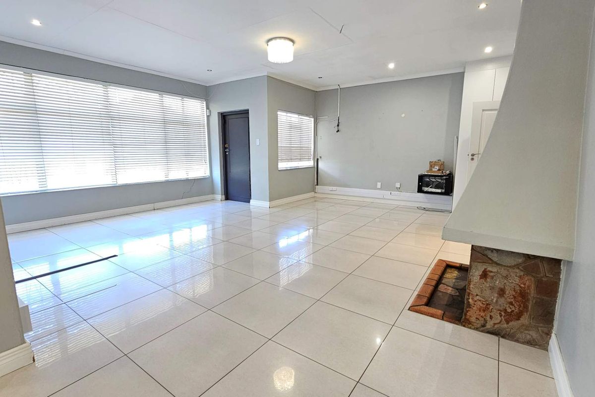 Spacious, empty living room featuring large format floor tiles, a traditional fireplace, and neutral wall finishes with natural light from large windows.