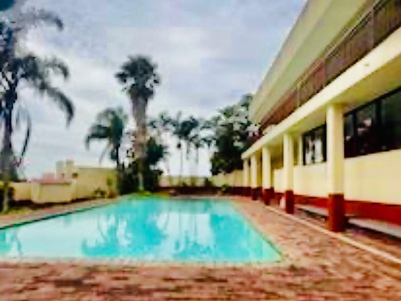 Outdoor swimming pool area featuring brick paving and a covered patio space adjacent to the apartment building.