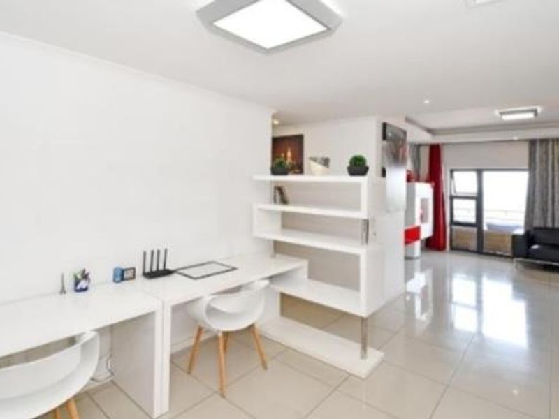 Spacious open-plan living area featuring a built-in study nook with integrated shelving, tiled floors, and direct access to a balcony through sliding glass doors.