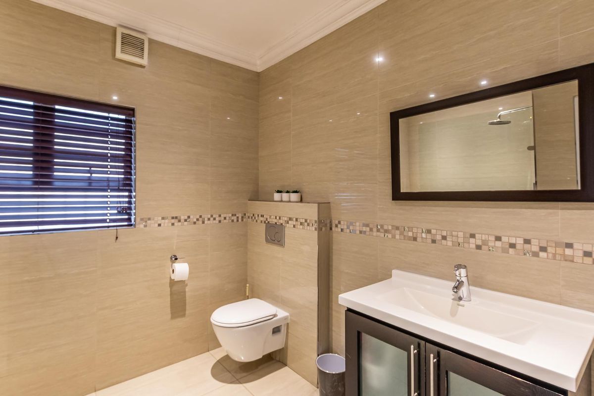 Modern bathroom featuring a wall-mounted toilet, vanity cabinet with basin, and neutral floor-to-ceiling wall tiles with a decorative mosaic border.