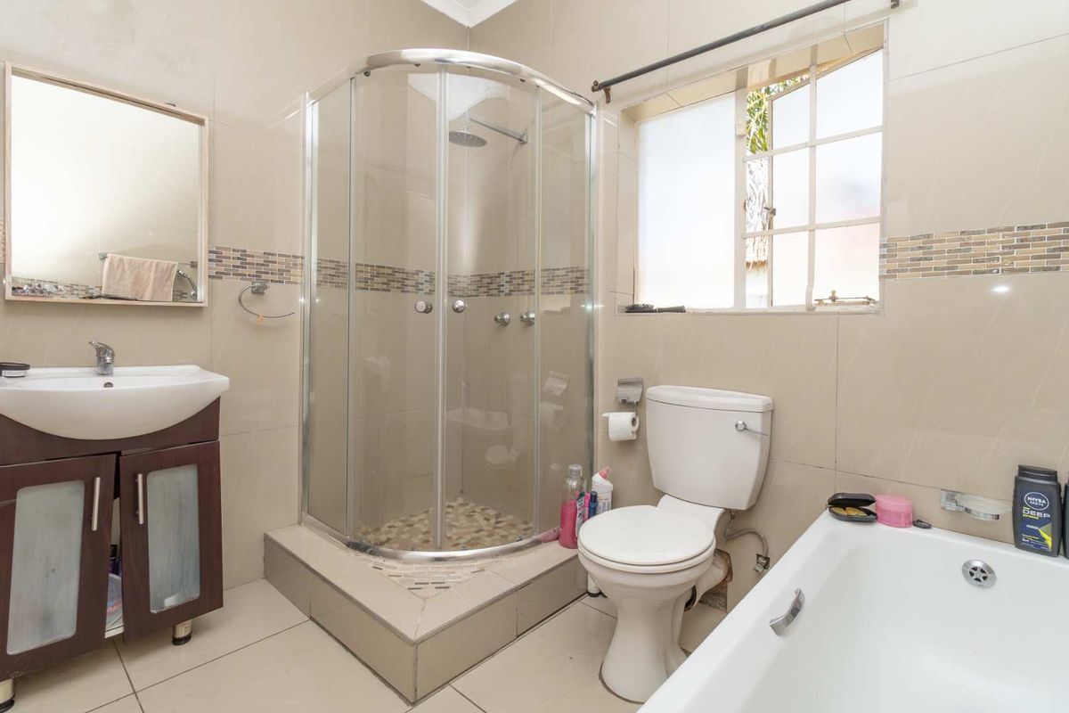 A functional bathroom featuring a corner shower enclosure, a bathtub, a vanity basin, and a toilet with neutral wall tiling.