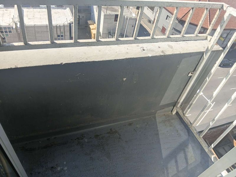 A compact apartment balcony featuring a metal balustrade and concrete parapet wall, showing signs of wear and surface staining.