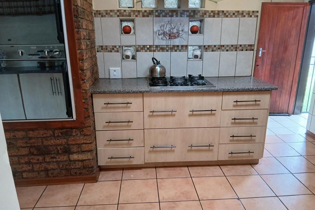 A functional kitchen featuring a gas hob, extractor fan, built-in oven, granite countertops, and a distinctive exposed brick feature wall.