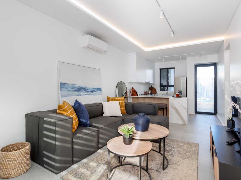 Modern open-plan living area featuring a sleek kitchen with stone island, recessed ceiling lighting, and tiled flooring, seamlessly connecting to the outdoor space.