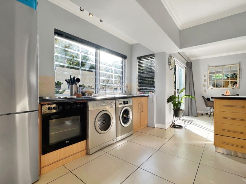 Functional kitchen featuring tiled flooring, built-in cabinetry, integrated oven and hob, and large windows with security bars, flowing into the adjacent living area.