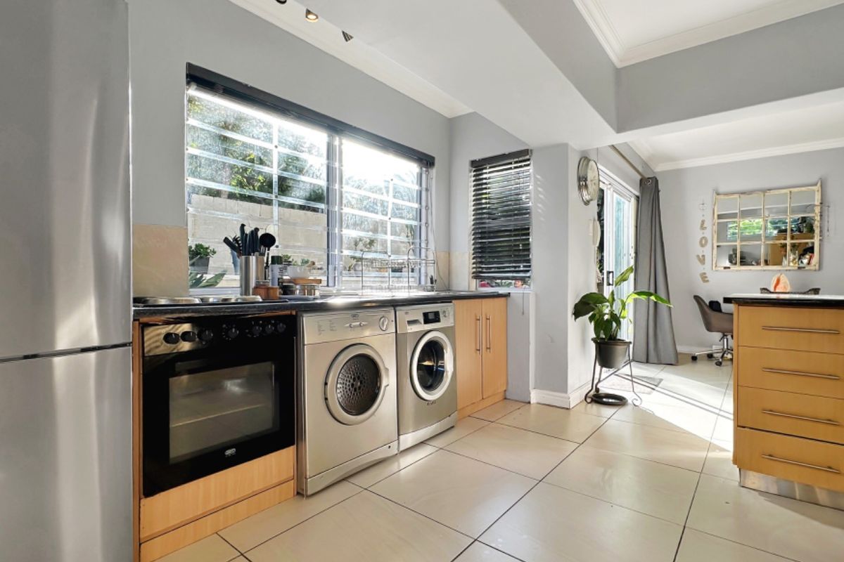 Functional kitchen featuring tiled flooring, built-in cabinetry, integrated oven and hob, and large windows with security bars, flowing into the adjacent living area.