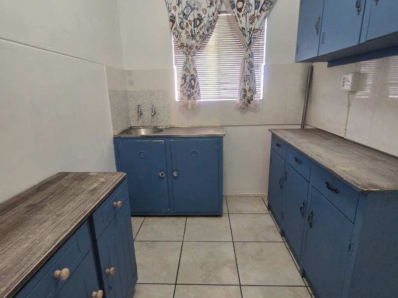 A functional kitchen space featuring blue built-in cabinetry, laminate countertops, and tiled flooring, offering a blank canvas for potential modern renovation.