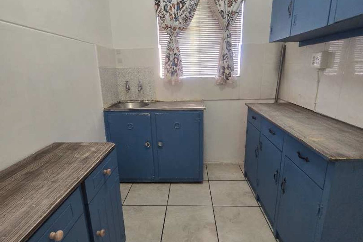 A functional kitchen space featuring blue built-in cabinetry, laminate countertops, and tiled flooring, offering a blank canvas for potential modern renovation.
