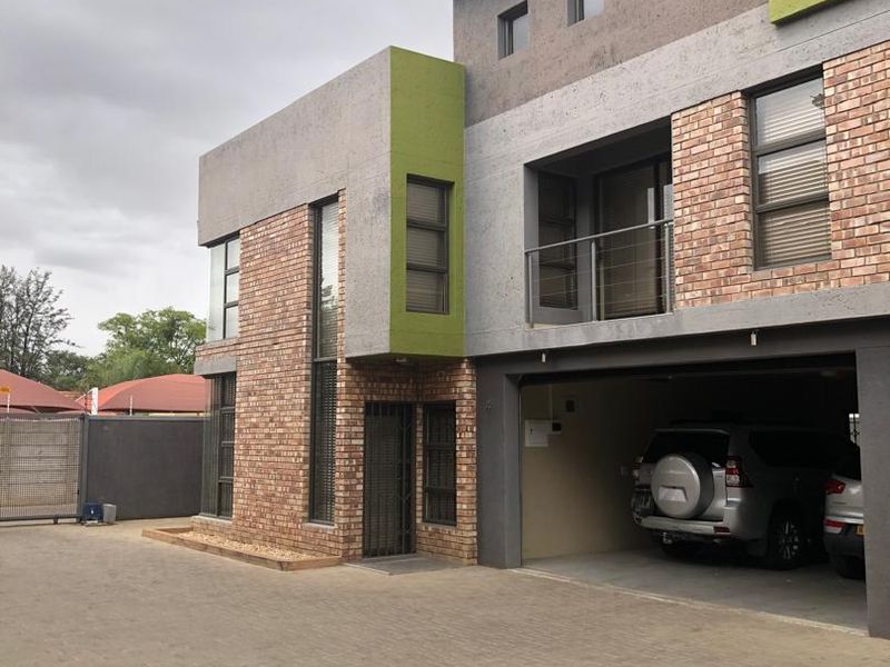 Modern townhouse exterior featuring a combination of face brick and rendered concrete finishes, including an integrated garage and an upper-level balcony.