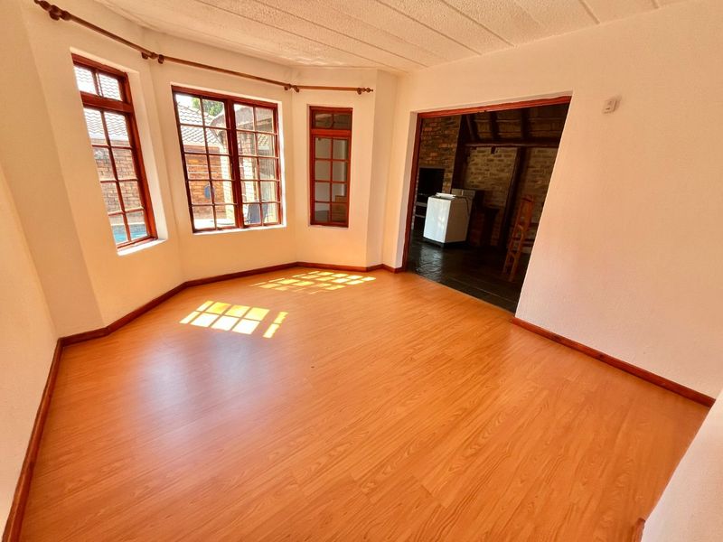 A bright, empty living room featuring laminate flooring, a bay window with wooden frames, and a textured ceiling, leading into an adjacent tiled area.