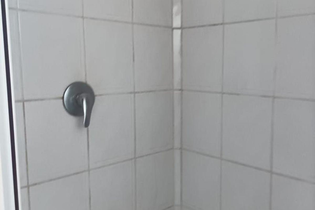 A compact shower enclosure featuring white wall tiles and a mosaic tiled floor base with a standard shower mixer.