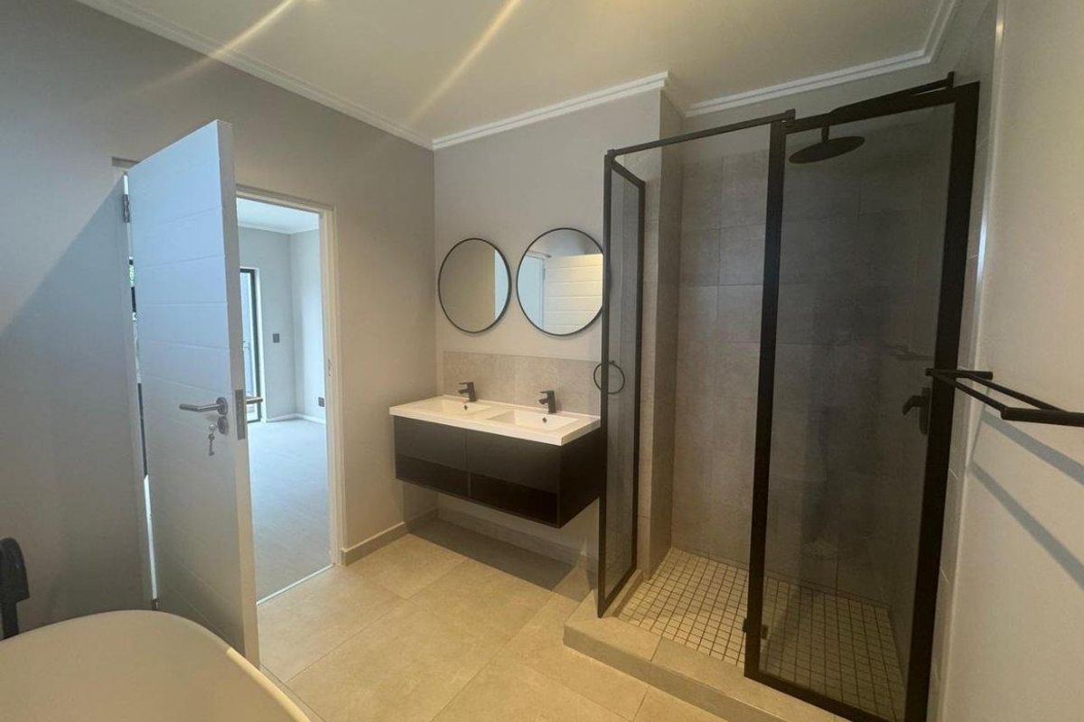 Modern bathroom featuring a double vanity, walk-in shower with black frame, and a freestanding bathtub.