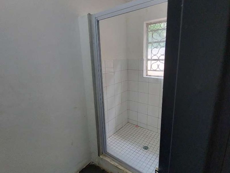 A small bathroom featuring a tiled shower enclosure with a glass door and a window, currently in need of cosmetic updates and floor finishing.
