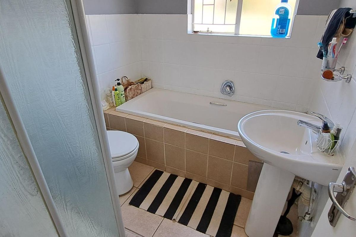 A functional bathroom featuring a bathtub, pedestal basin, and toilet with tiled finishes and a window providing natural light.