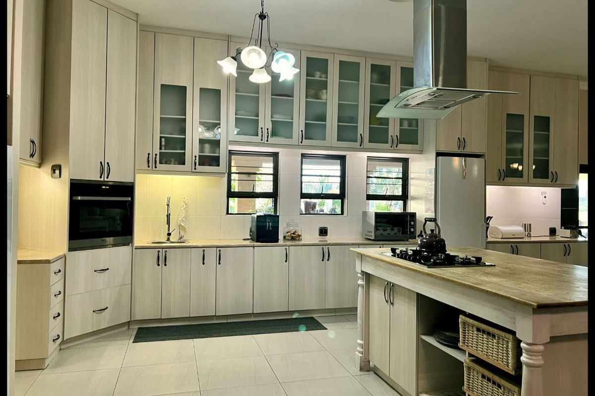 Modern kitchen featuring light wood cabinetry, a central island with a built-in gas hob, stainless steel extractor fan, and tiled flooring.