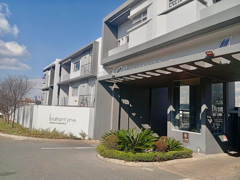 The front entrance and security gate of the Ballantyne apartment complex in Bryanston, featuring modern architectural design and paved access.