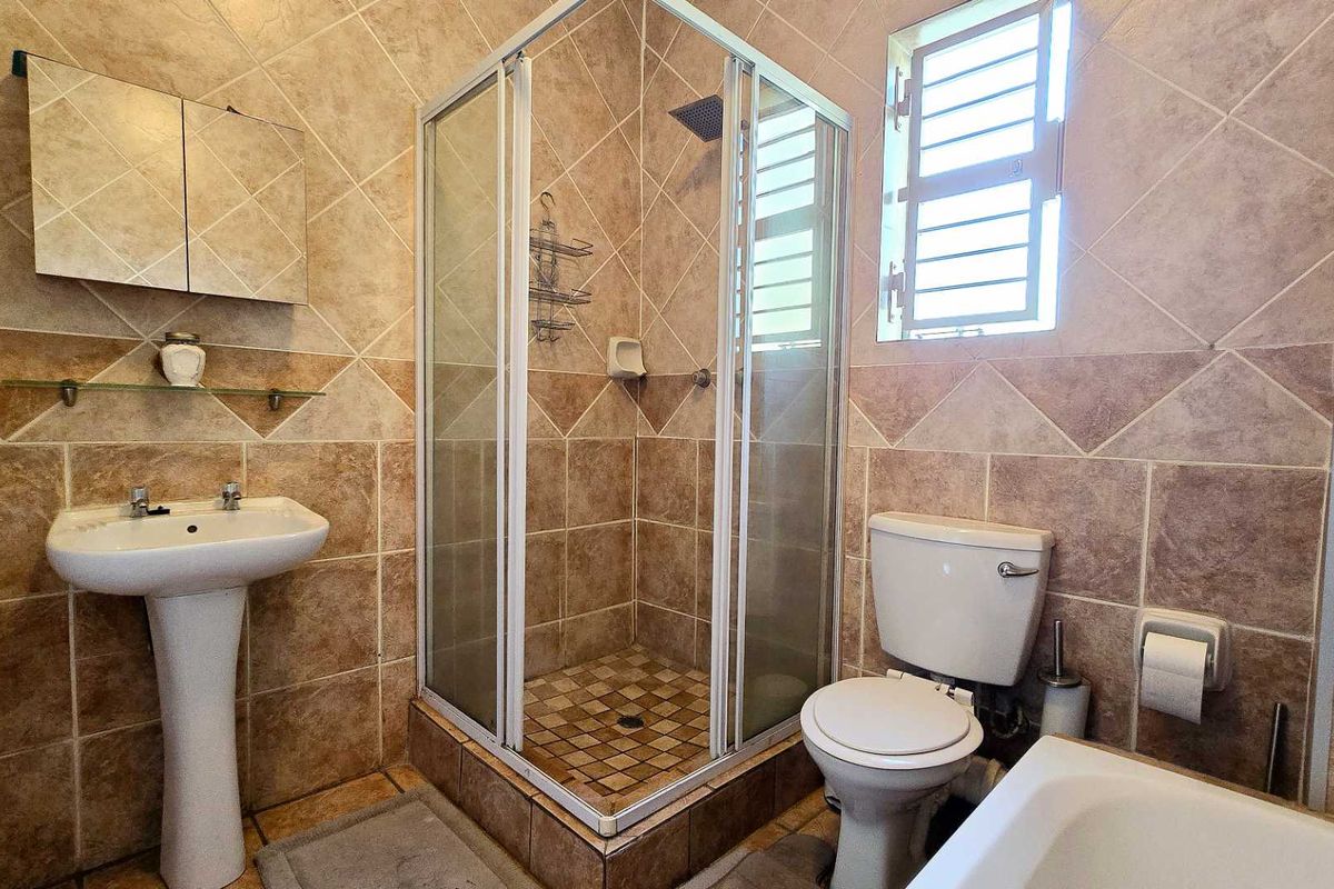 A functional bathroom featuring a corner shower enclosure, pedestal basin, and toilet, finished with full-height wall tiling and a window for natural ventilation.