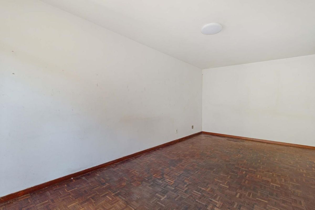 An empty bedroom featuring traditional parquet flooring and plain white walls, offering a blank canvas for renovation or interior design updates.