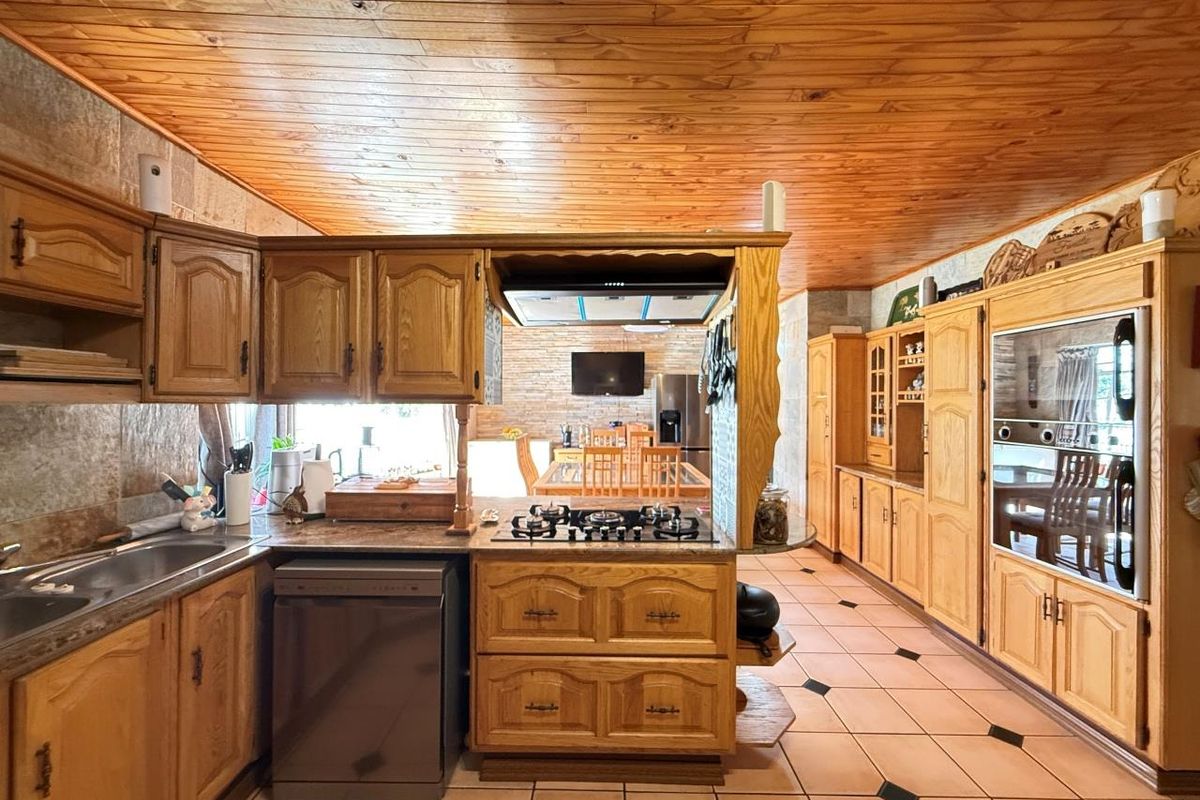 Spacious kitchen featuring extensive timber cabinetry, built-in oven, gas hob, extractor fan, and tiled flooring with a warm wood-paneled ceiling.