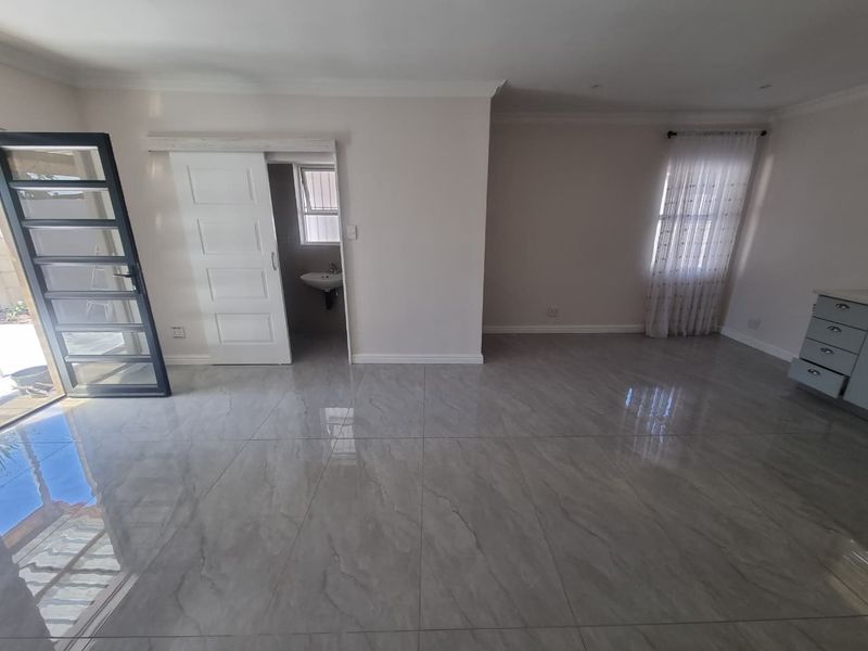 Spacious living area featuring large format porcelain floor tiles, neutral wall finishes, and direct access to an adjoining washroom area.
