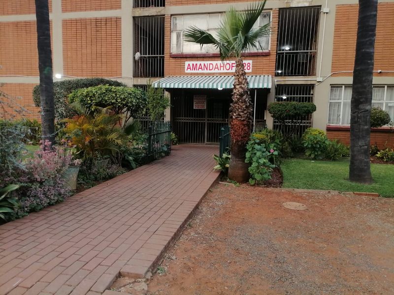 Front entrance view of the Amandahof apartment building featuring a brick facade, paved walkway, and secure gated access.