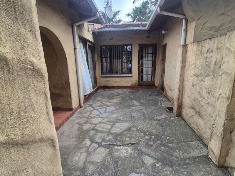 A private, enclosed courtyard patio featuring rustic flagstone paving, textured stucco walls, and direct access to the home through timber-framed doors and windows.