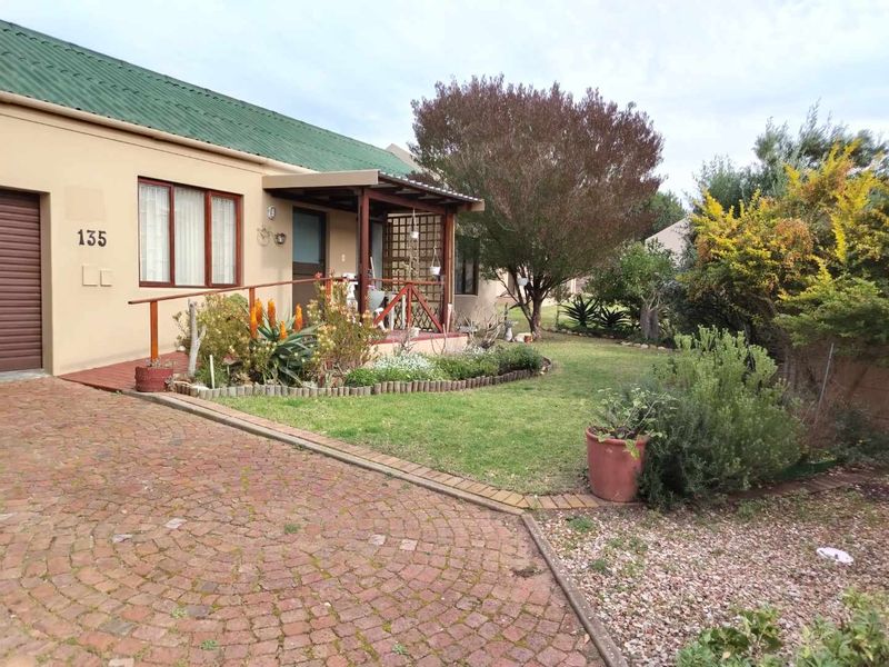 Front view of a townhouse featuring a paved driveway, covered entrance porch with timber railing, and a well-established garden area.