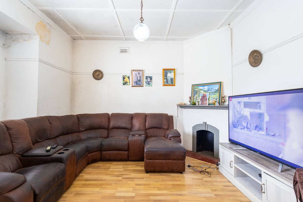 A living room featuring a fireplace, timber flooring, and a tiled ceiling, currently showing signs of wear and requiring cosmetic updates.