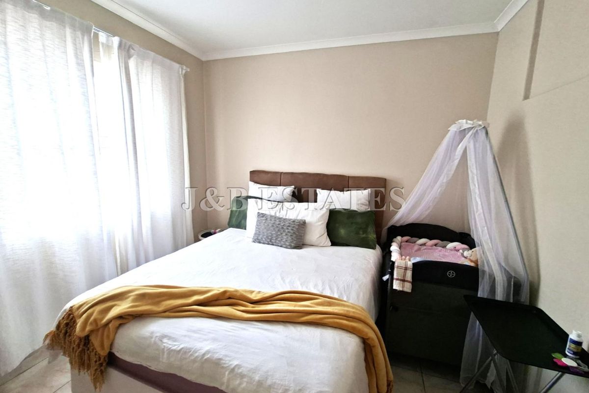 A functional bedroom featuring tiled flooring, neutral wall tones, and large windows allowing for natural light.