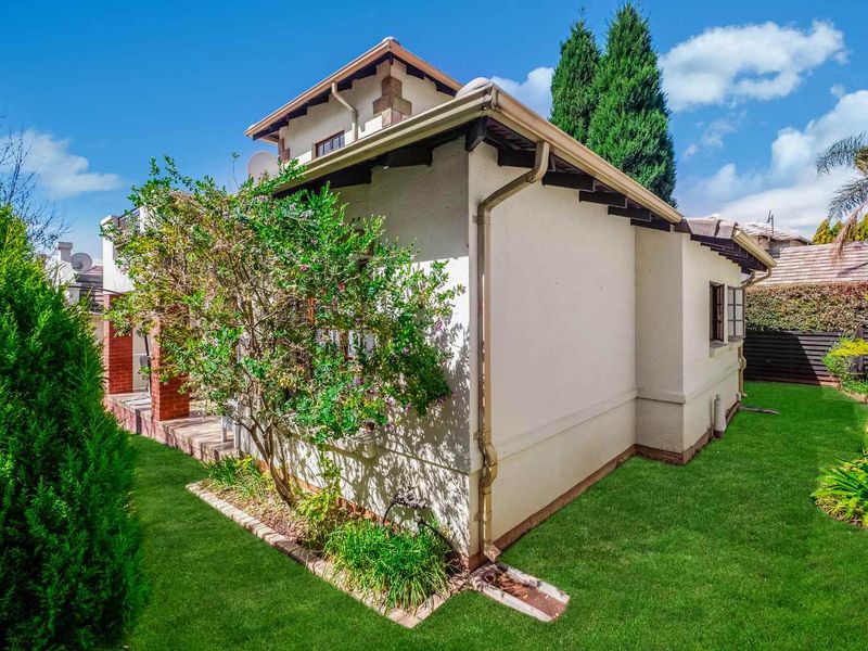 A well-maintained rear exterior view of the townhouse featuring a landscaped garden, tiled roof, and exposed rafter detailing.