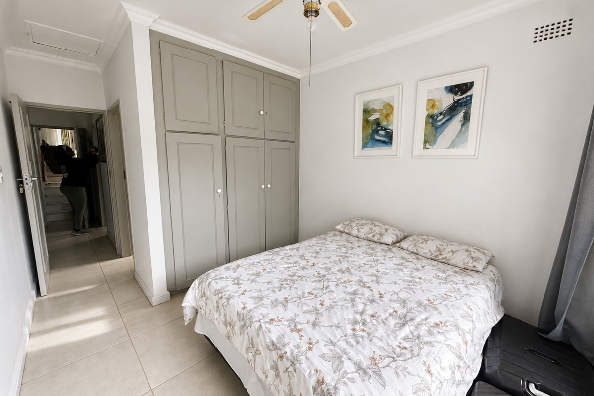 A well-maintained bedroom featuring neutral tiled flooring, built-in grey cabinetry, and a ceiling fan, offering a clean and functional living space.