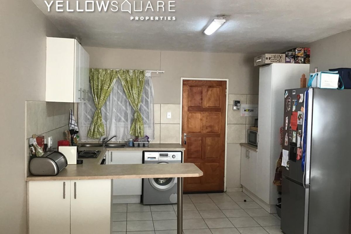 Functional kitchen featuring built-in cabinetry, laminate countertops, tiled backsplash, and integrated laundry plumbing, offering a practical layout for daily use.