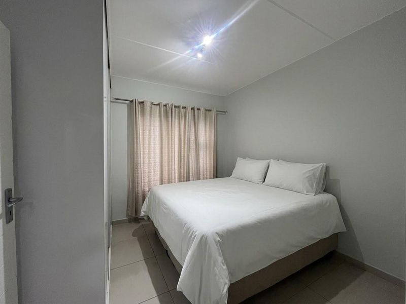 A clean and functional bedroom featuring neutral tiled flooring, a built-in wardrobe, and a window with installed curtain rod.