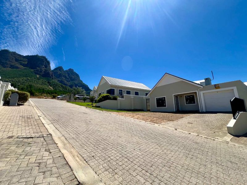 Front exterior view of a residential property featuring a paved driveway, garage, and mountain backdrop in a clear, sunny setting.
