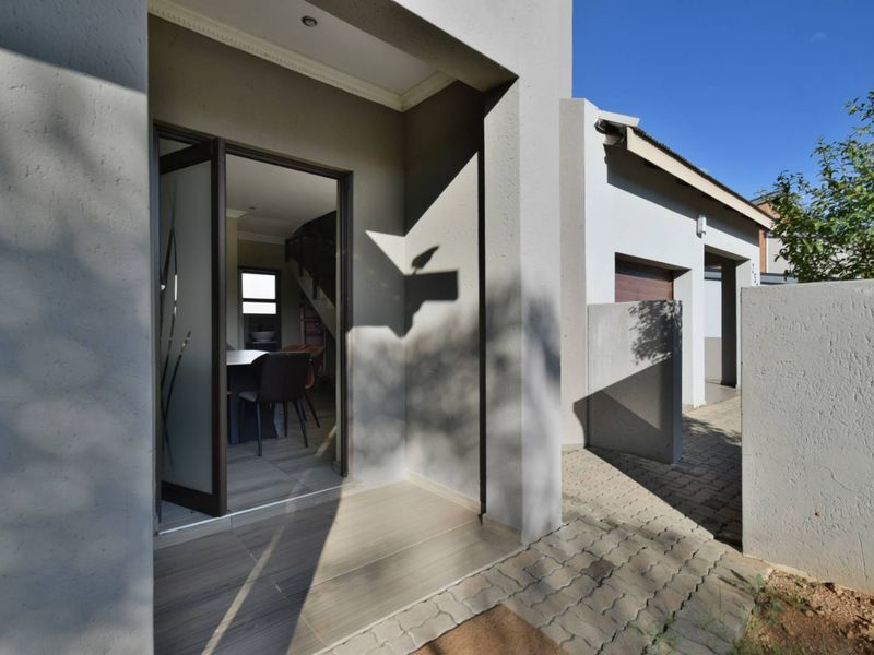 A modern front entrance featuring a covered porch, paved driveway, and a glass-panelled door leading into the home.