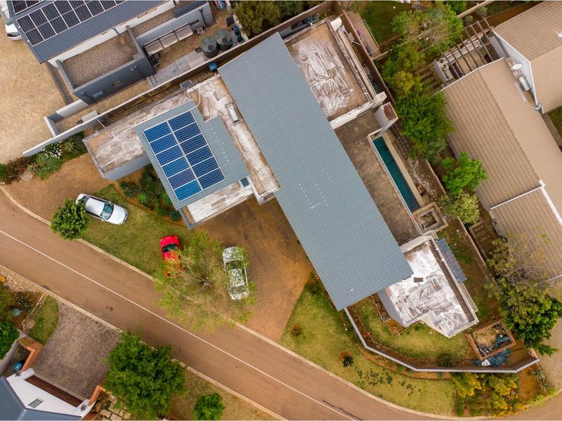 Aerial view of the property showcasing the metal roof, integrated solar panel system, paved driveway, and a narrow lap pool.
