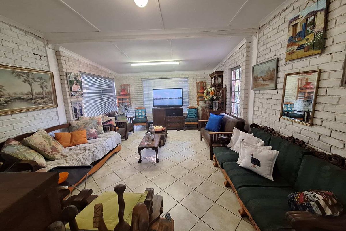 Spacious living room featuring white painted brick walls, tiled flooring, and large windows providing natural light.