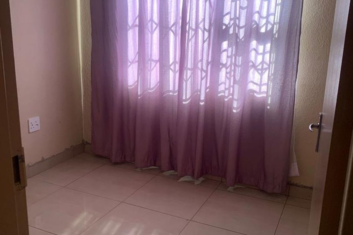 A compact bedroom featuring tiled flooring and a large window with curtaining, providing a neutral space ready for personalization.