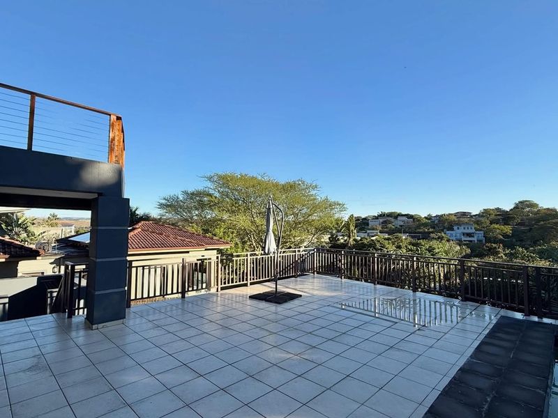 Spacious elevated patio featuring tiled flooring, metal balustrades, and an adjoining swimming pool with scenic neighborhood views.