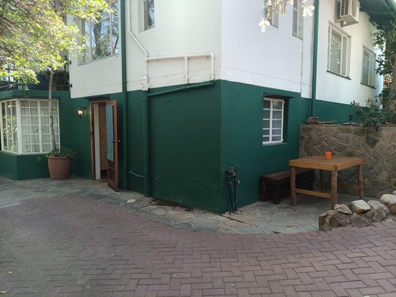 A rear exterior view of the apartment featuring a paved patio area, stone retaining wall, and painted exterior walls with integrated lighting and air conditioning.