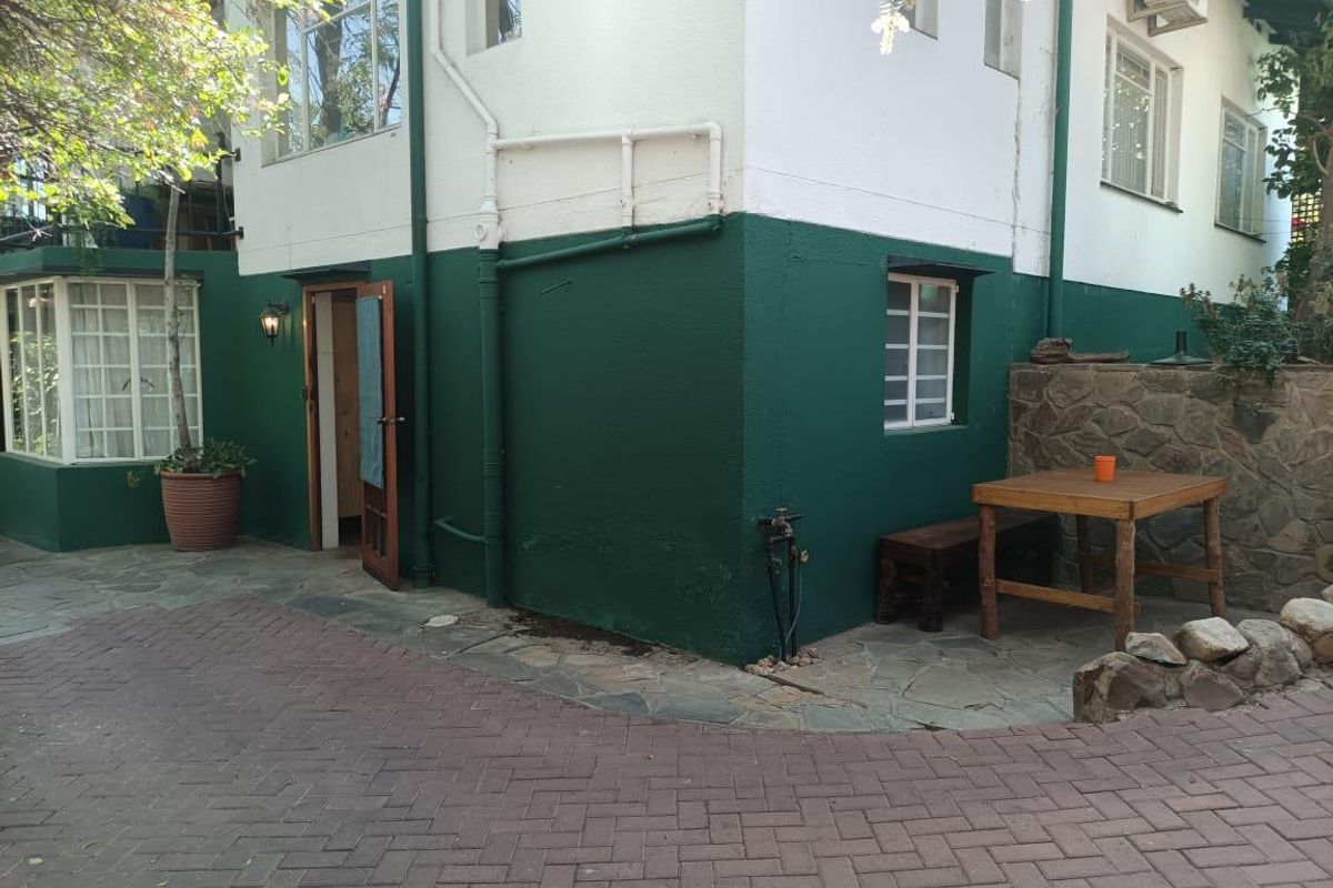 A rear exterior view of the apartment featuring a paved patio area, stone retaining wall, and painted exterior walls with integrated lighting and air conditioning.