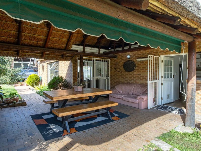 A covered outdoor patio area featuring a thatched roof, brick paving, and a built-in braai, providing a functional space for outdoor entertaining.