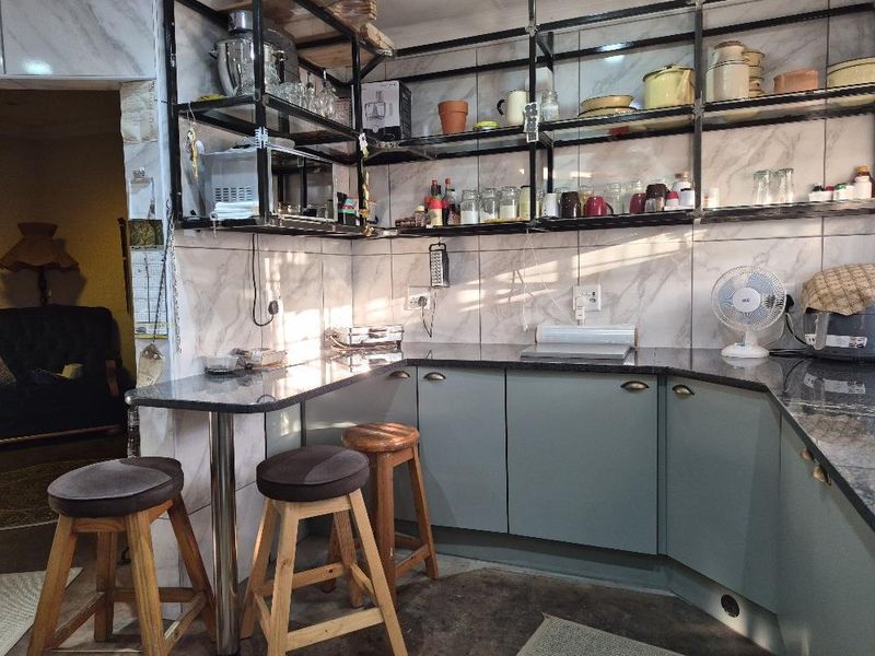 A functional kitchen area featuring granite countertops, open metal shelving, and tiled walls with integrated cabinetry.
