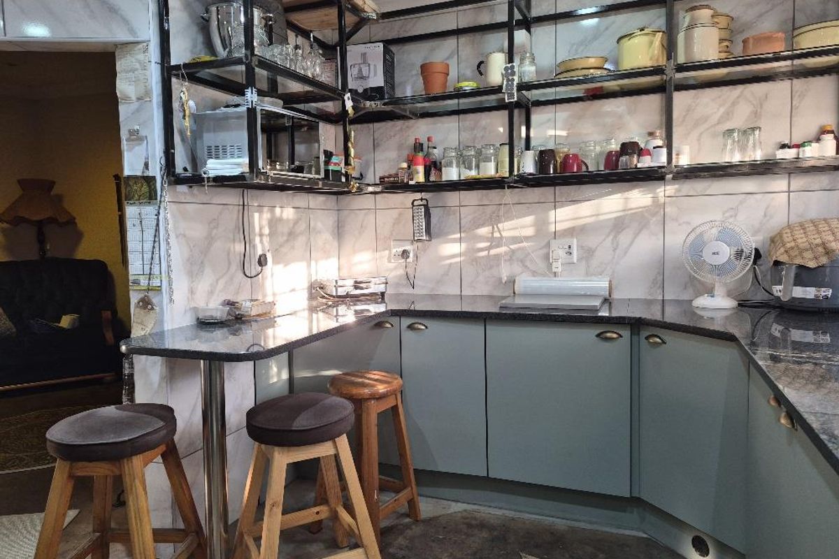 A functional kitchen area featuring granite countertops, open metal shelving, and tiled walls with integrated cabinetry.