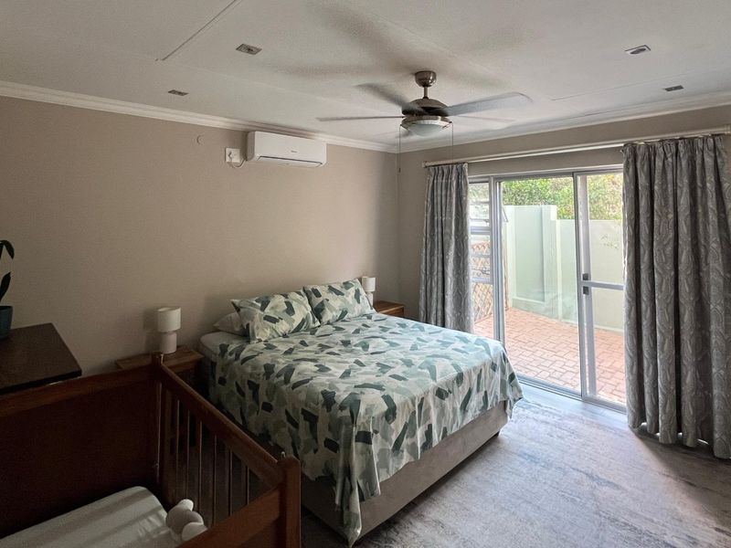 A well-maintained bedroom featuring laminate flooring, a ceiling fan, split-system air conditioning, and direct access to an outdoor patio through sliding glass doors.
