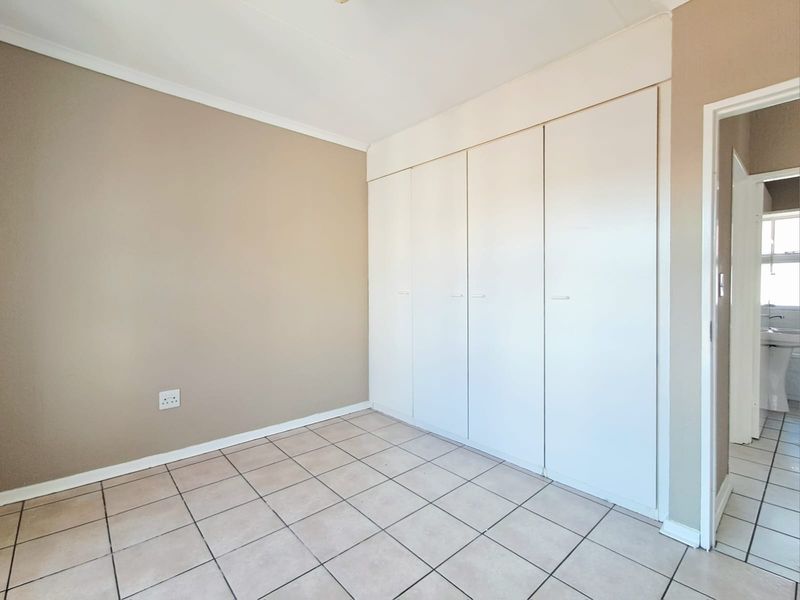 A clean, empty bedroom featuring neutral wall tones, tiled flooring, and ample built-in cupboard storage space.
